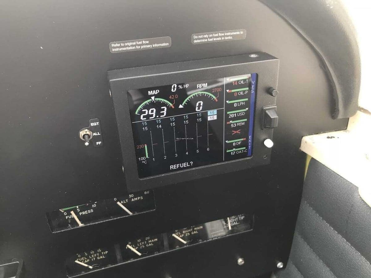 Close-up of a digital engine monitor display and analog gauges in an aircraft cockpit.