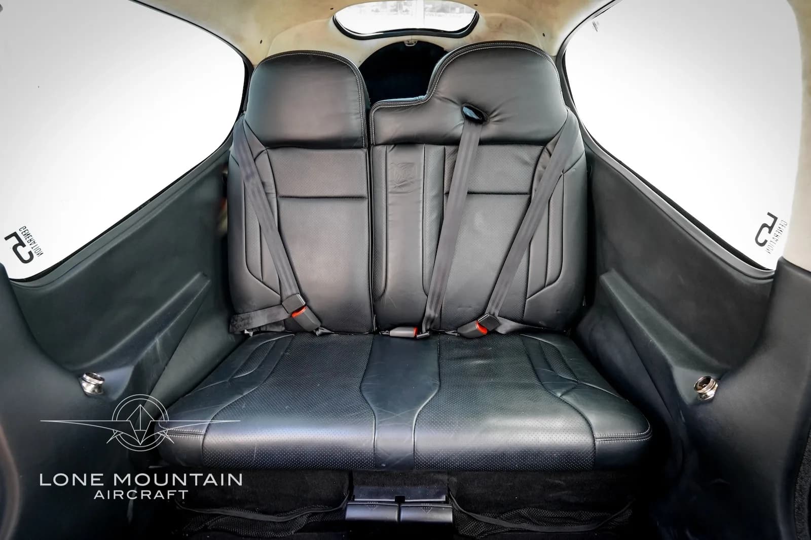 The black leather rear bench seat of the Cirrus SR22 aircraft cabin, with seatbelts visible.