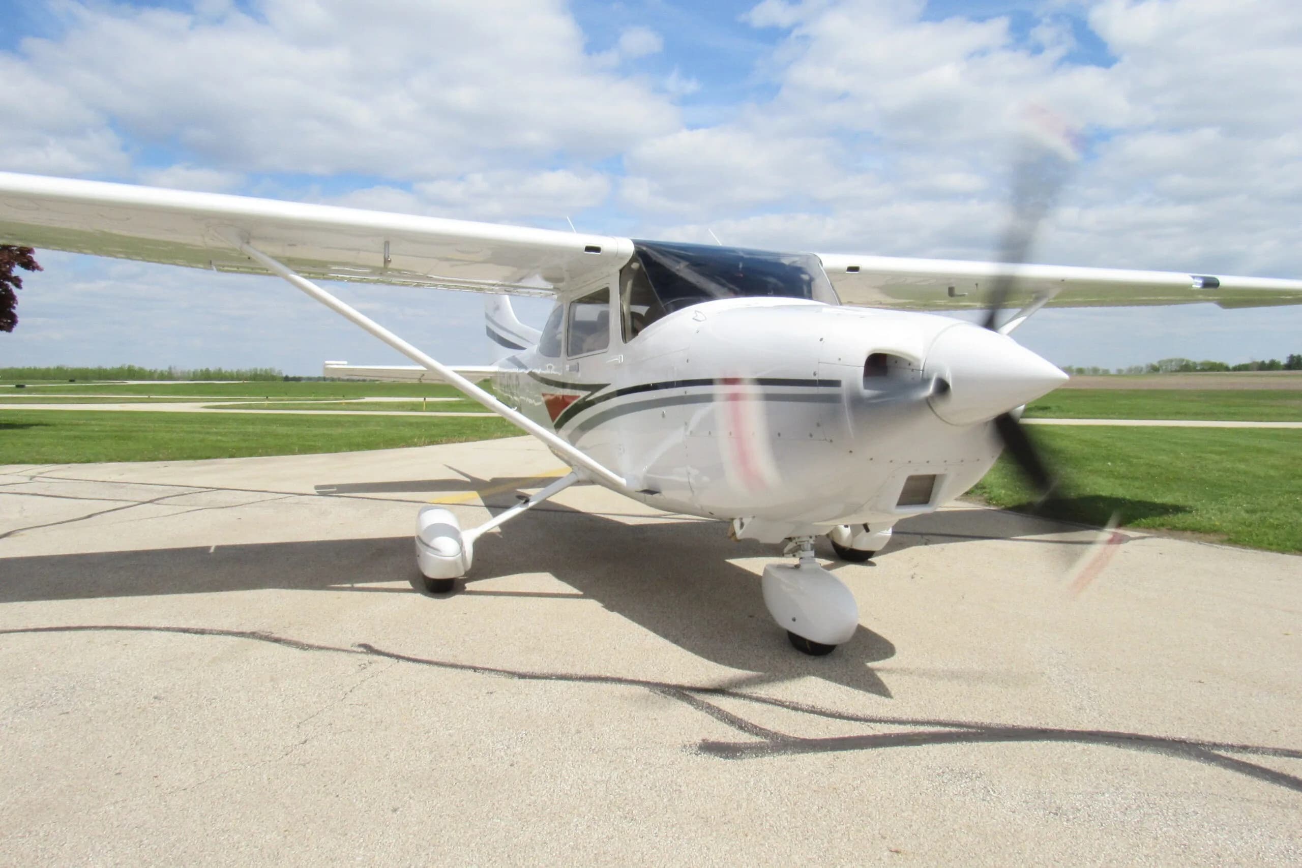 A white single-engine propeller aircraft with a spinning propeller is parked on an airport tarmac.