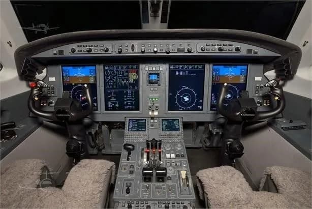 The cockpit of a private jet, displaying multiple digital screens, control yokes, and a central control panel.
