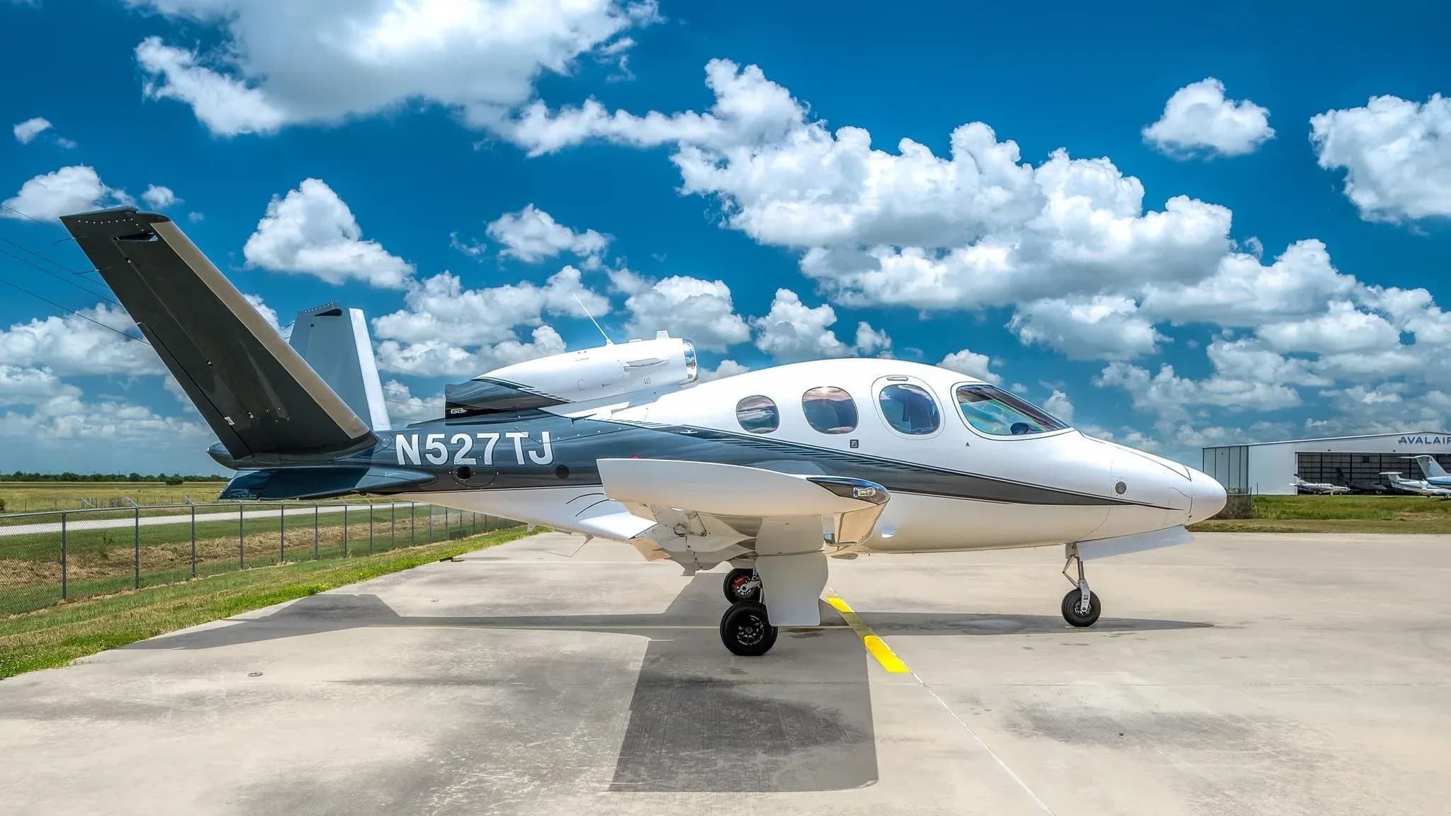 A white and dark grey Cirrus Vision Jet (SF50) with registration N527TJ parked on a tarmac under a blue sky.