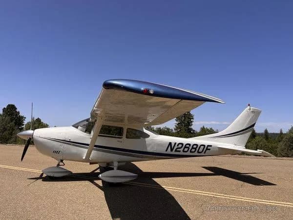A white single-engine propeller aircraft with blue wing accents and registration N2680F, parked on an asphalt surface under a clear blue sky, viewed from the front-right.
