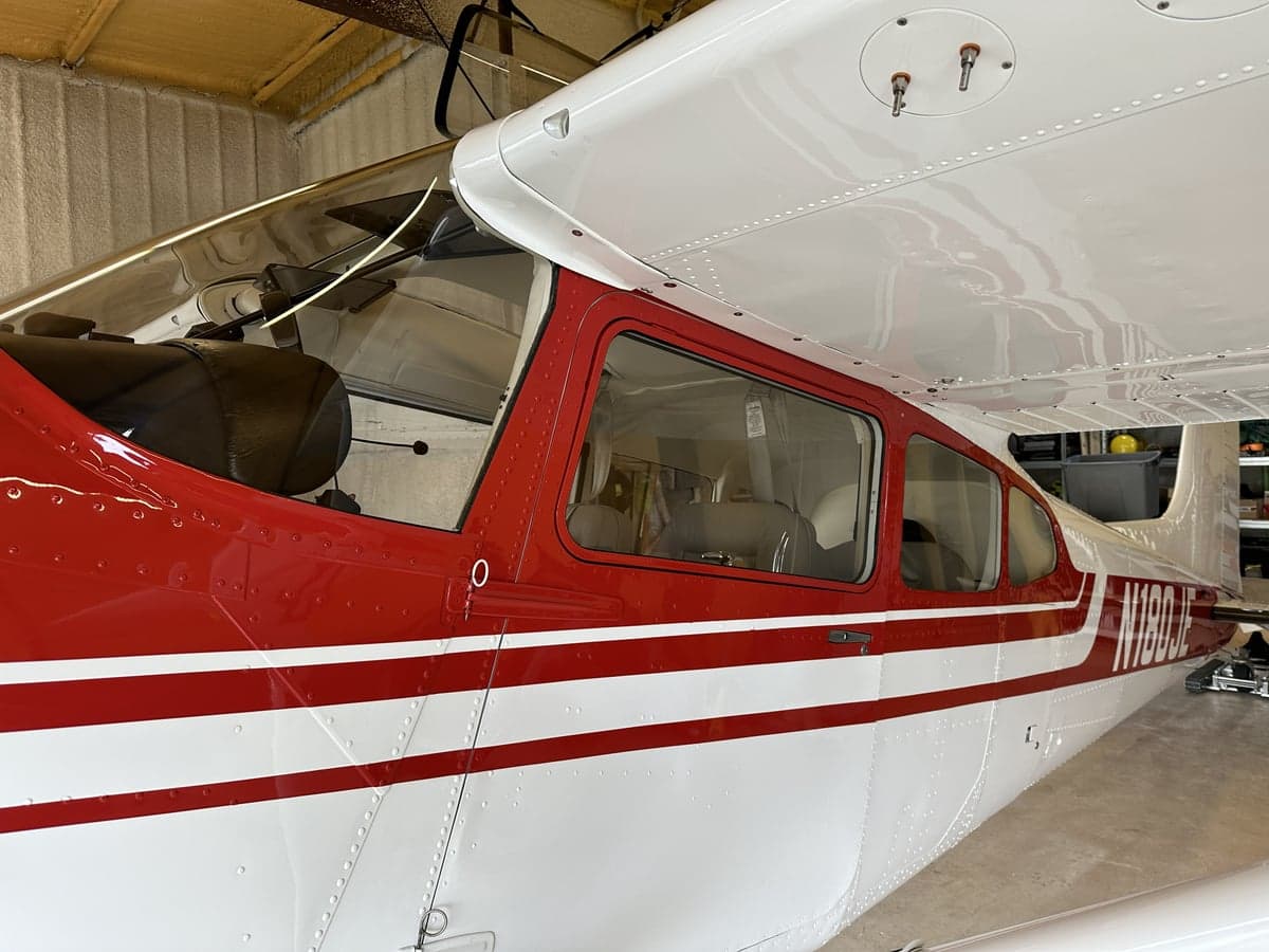 Side view of N180JE in a hangar.