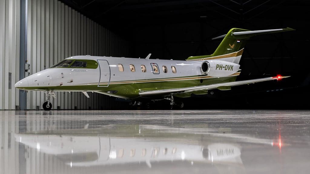 A white and green business jet, registration PH-DVK, parked in a hangar.