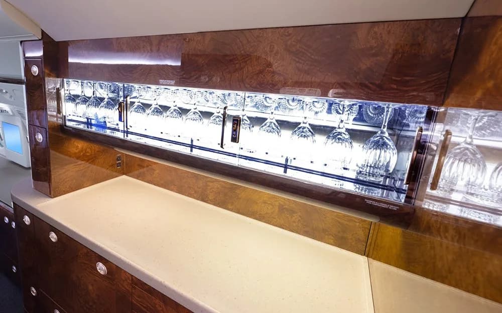 A well-lit bar area in a private jet, displaying rows of sparkling glassware.