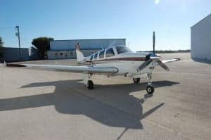 A Beechcraft Bonanza sits on the tarmac in the sun.