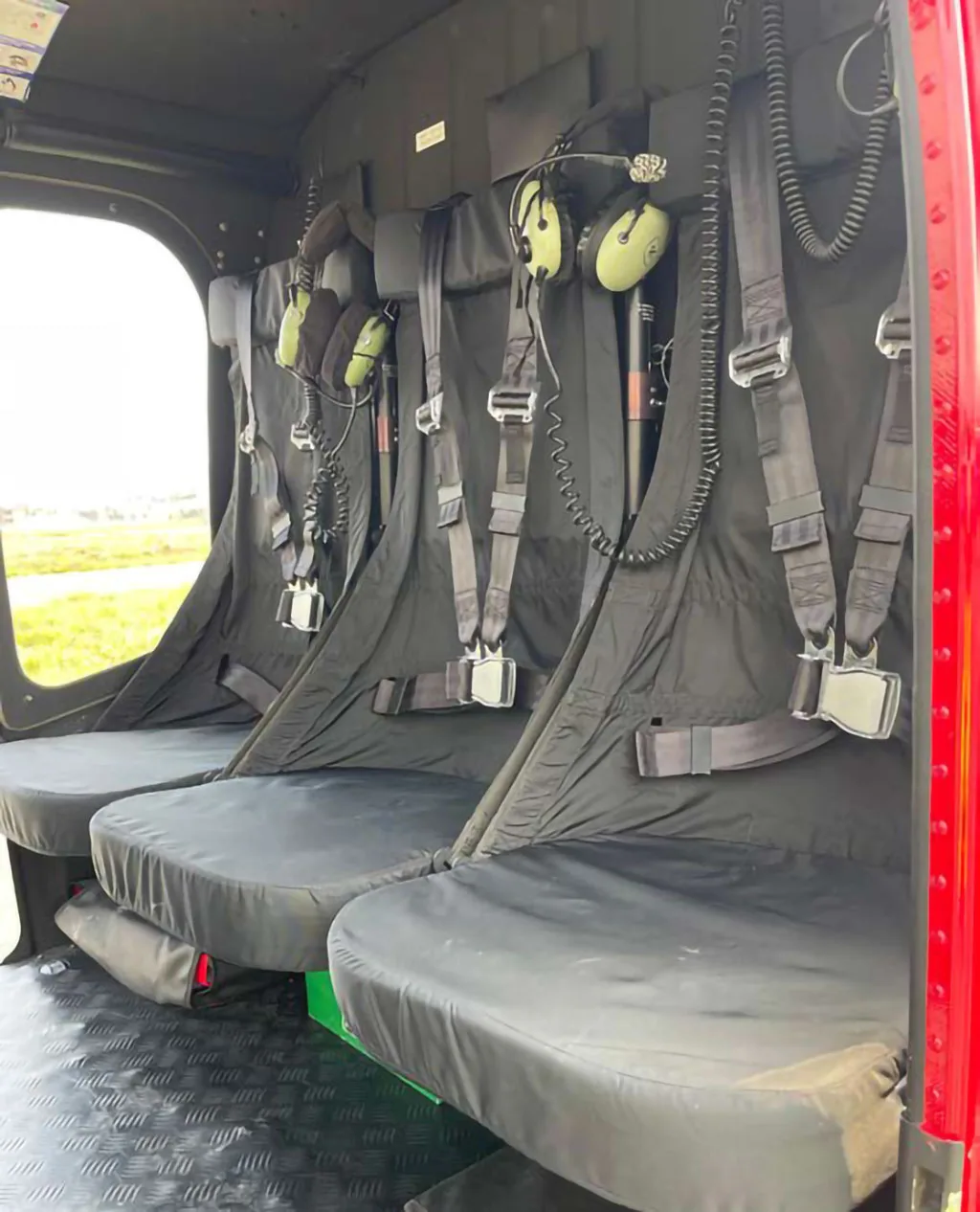 Three black passenger seats with safety harnesses and headsets are visible in the helicopter's cabin.