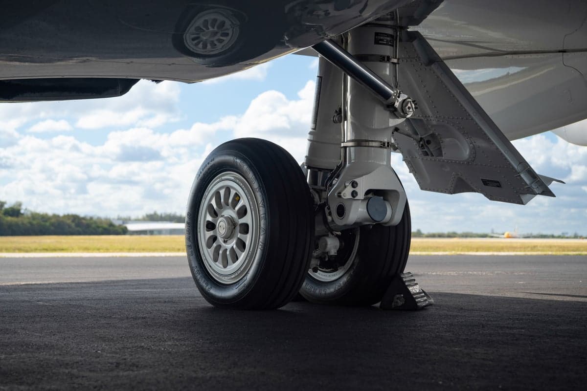 A close-up view of the main landing gear and wheels of a business jet on an asphalt runway.