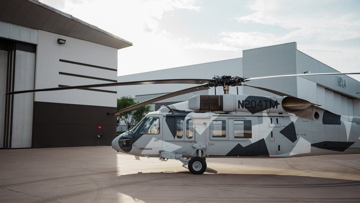 Side view of a Sikorsky S-70i helicopter with a gray camouflage paint scheme on the tarmac.