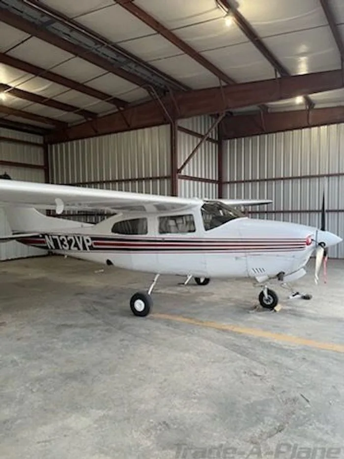 A white single-engine propeller aircraft with red and black stripes, registration N732VP, parked inside a metal hangar.