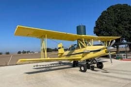 A yellow biplane crop duster sits on the tarmac under a blue sky.