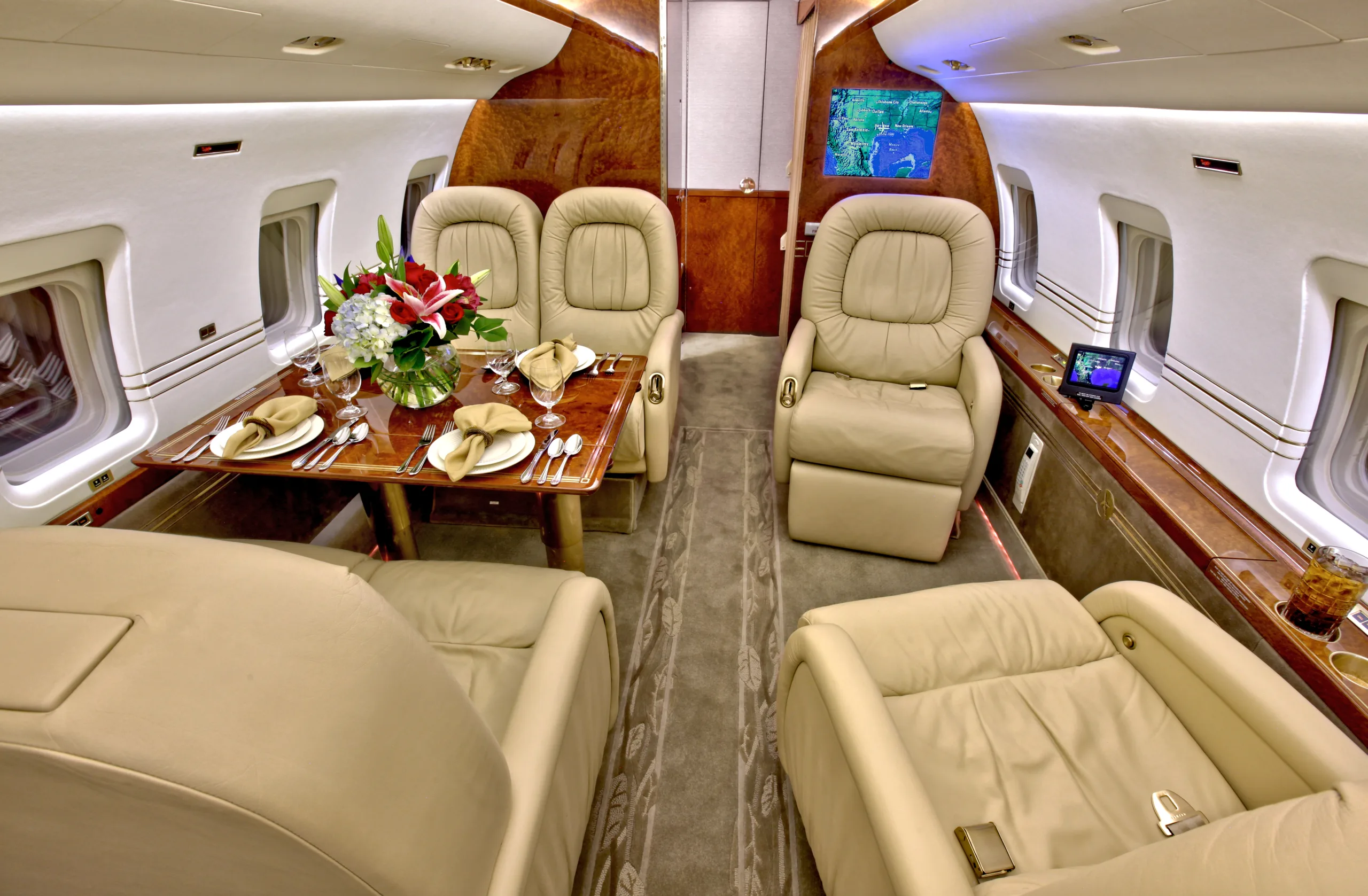 The luxurious interior of a private jet cabin with beige leather seats and a dining table set with flowers.