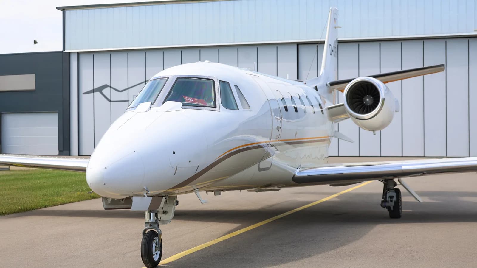 A white Cessna Citation private jet with registration D-CEHM is parked head-on in front of a modern hangar.