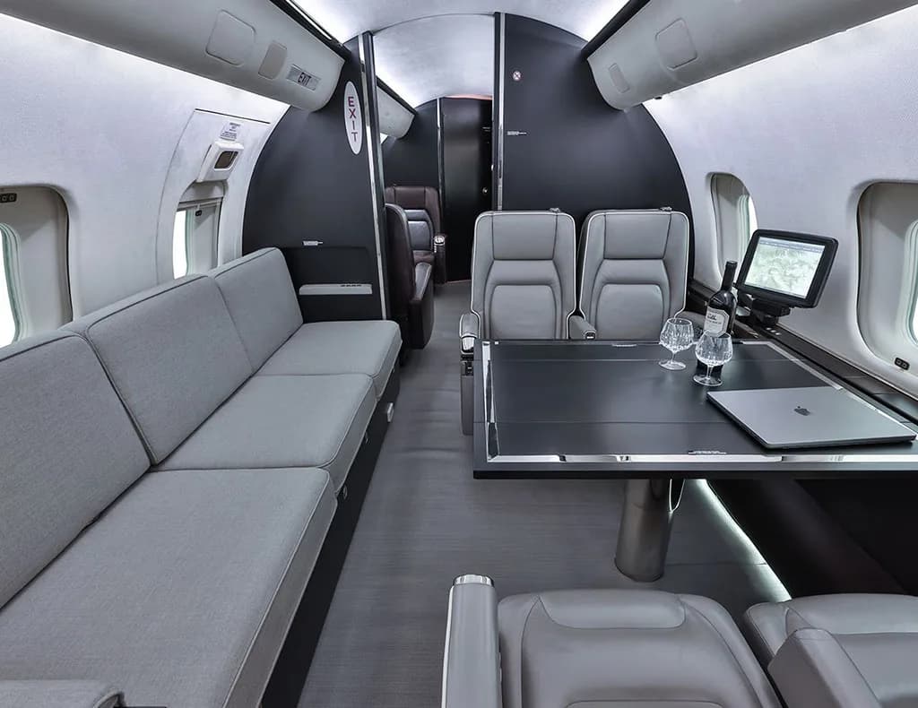 A luxurious private jet interior featuring a grey sofa, a dark table with drinks, and additional seating.