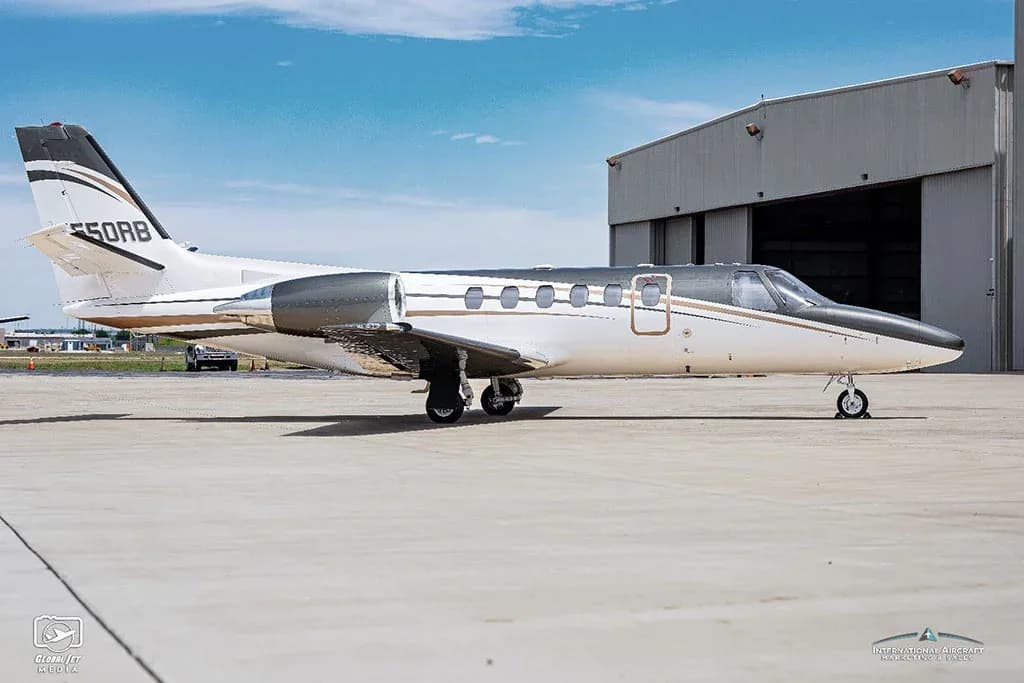 A white and dark grey Cessna Citation V (N550RB) business jet is parked on a tarmac next to a large hangar.