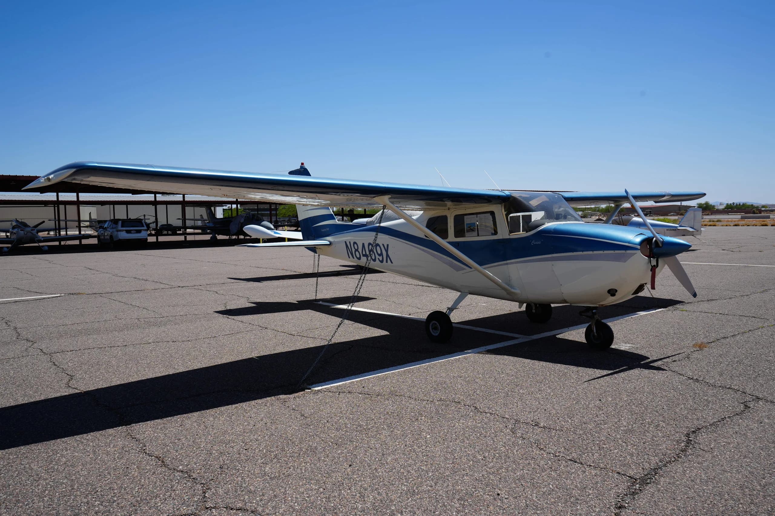 Side view of a white and blue Cessna 172 (N8469X) with its propeller facing right, parked on an airfield.