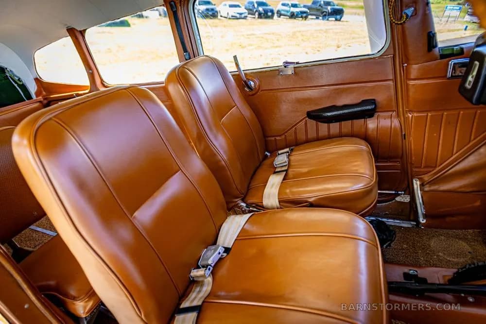 The brown leather passenger seats in the cabin of a small aircraft, with a view of cars outside the window.