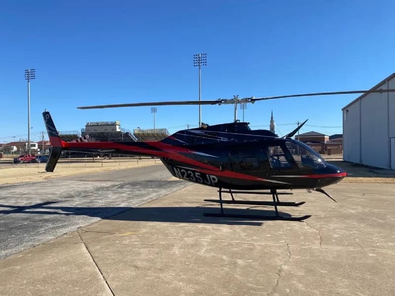 Bell 206L-4 helicopter, registration N235JP, parked on a concrete pad with a black and red paint scheme.