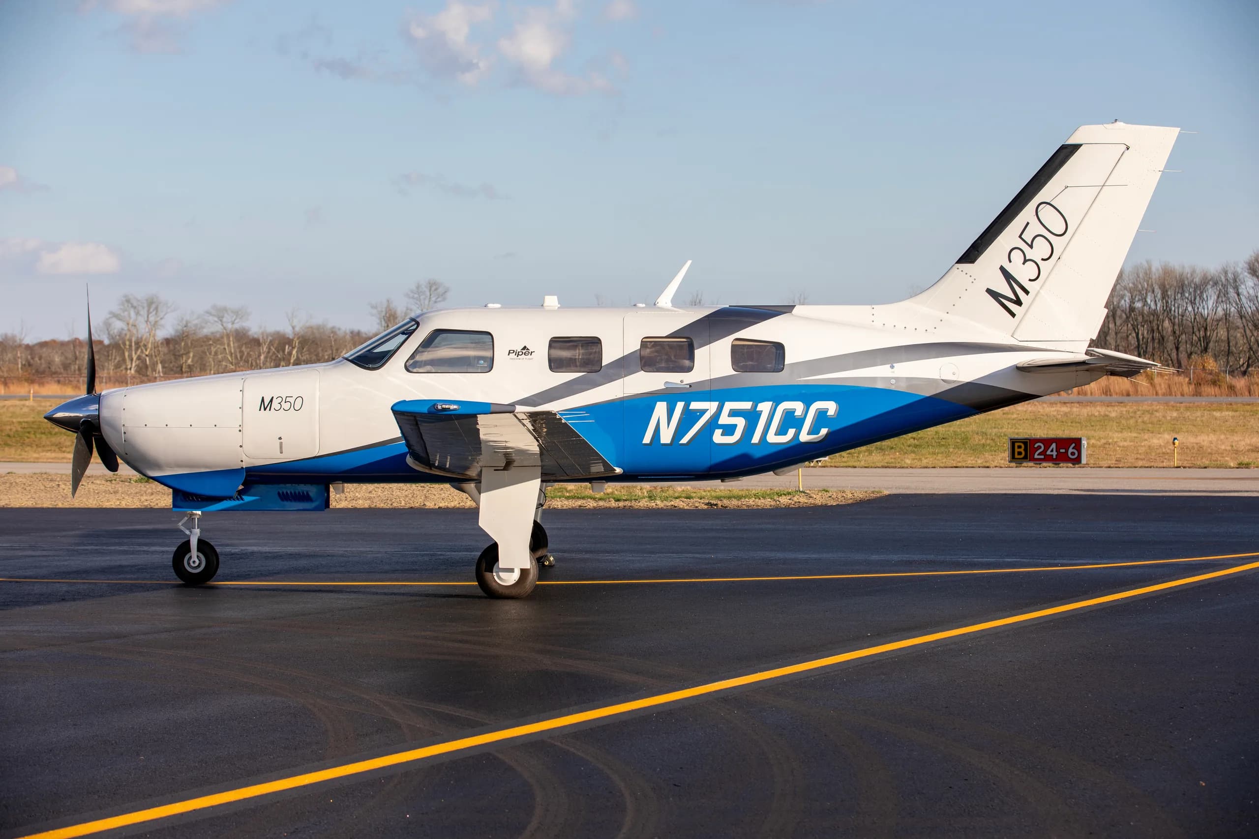 A side view of a Piper M350 aircraft, registration N751CC, with a white and blue paint scheme, parked on an airfield.