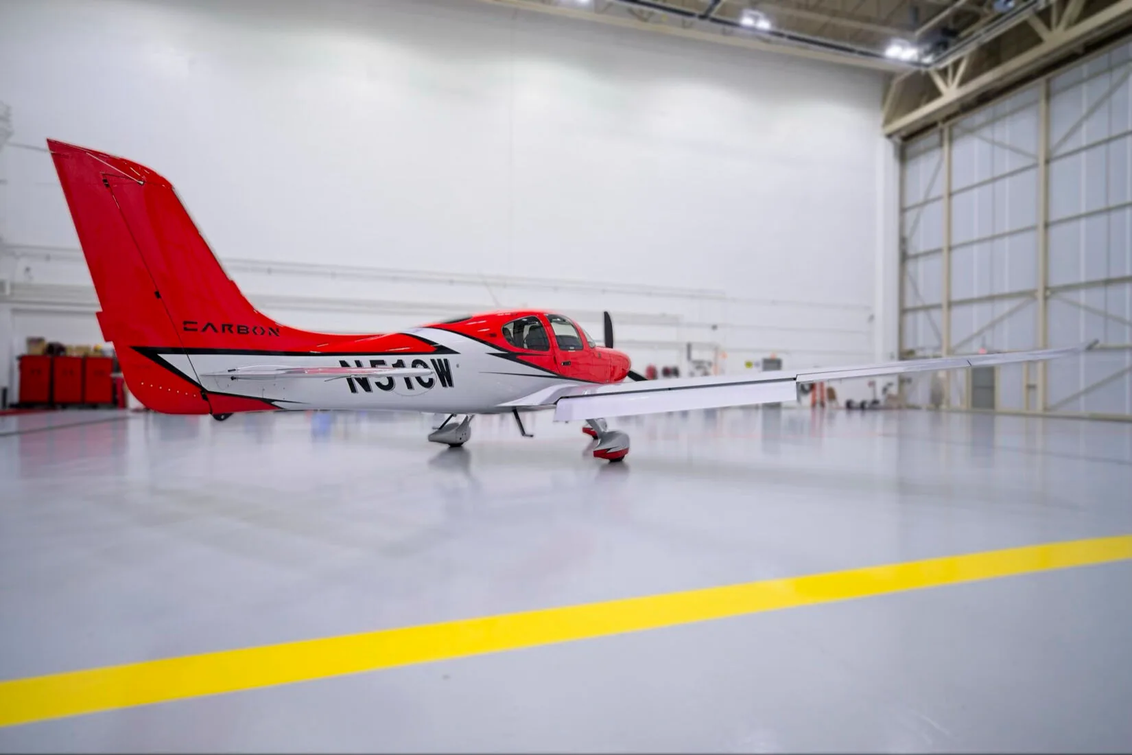 A side view of a red and white Cirrus SR22 aircraft with registration N51CW in a hangar, showing the full wing span.