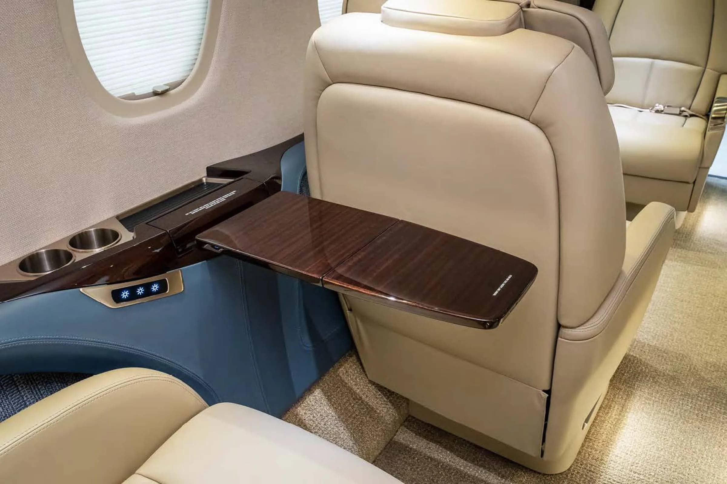 A close-up of a beige leather aircraft seat with a folded-out polished wooden table and cup holders.