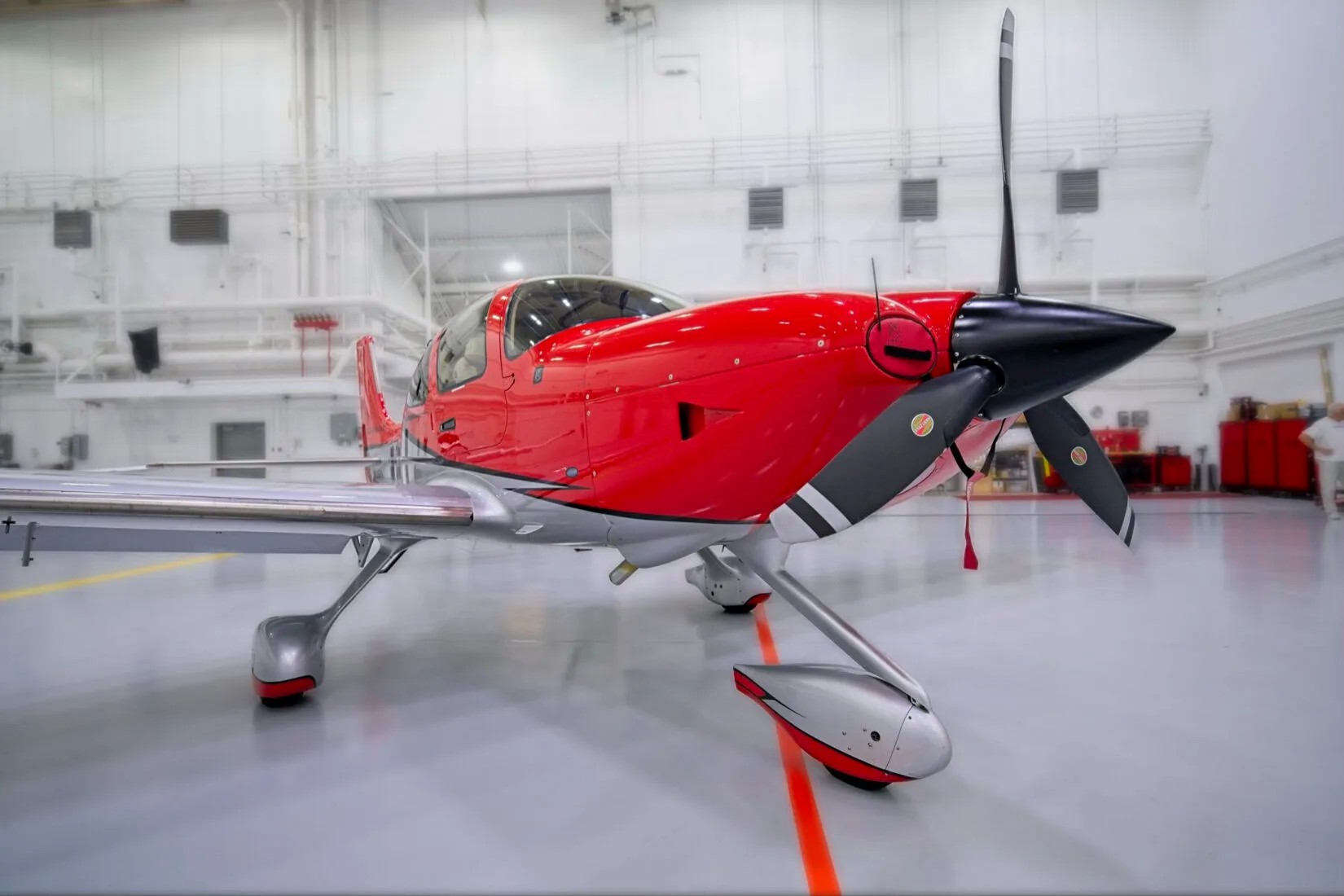 A close-up front view of the propeller and nose of a red and white Cirrus SR22 aircraft in a hangar.