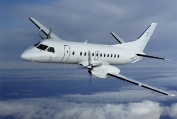 A white turboprop aircraft flies through the clouds.