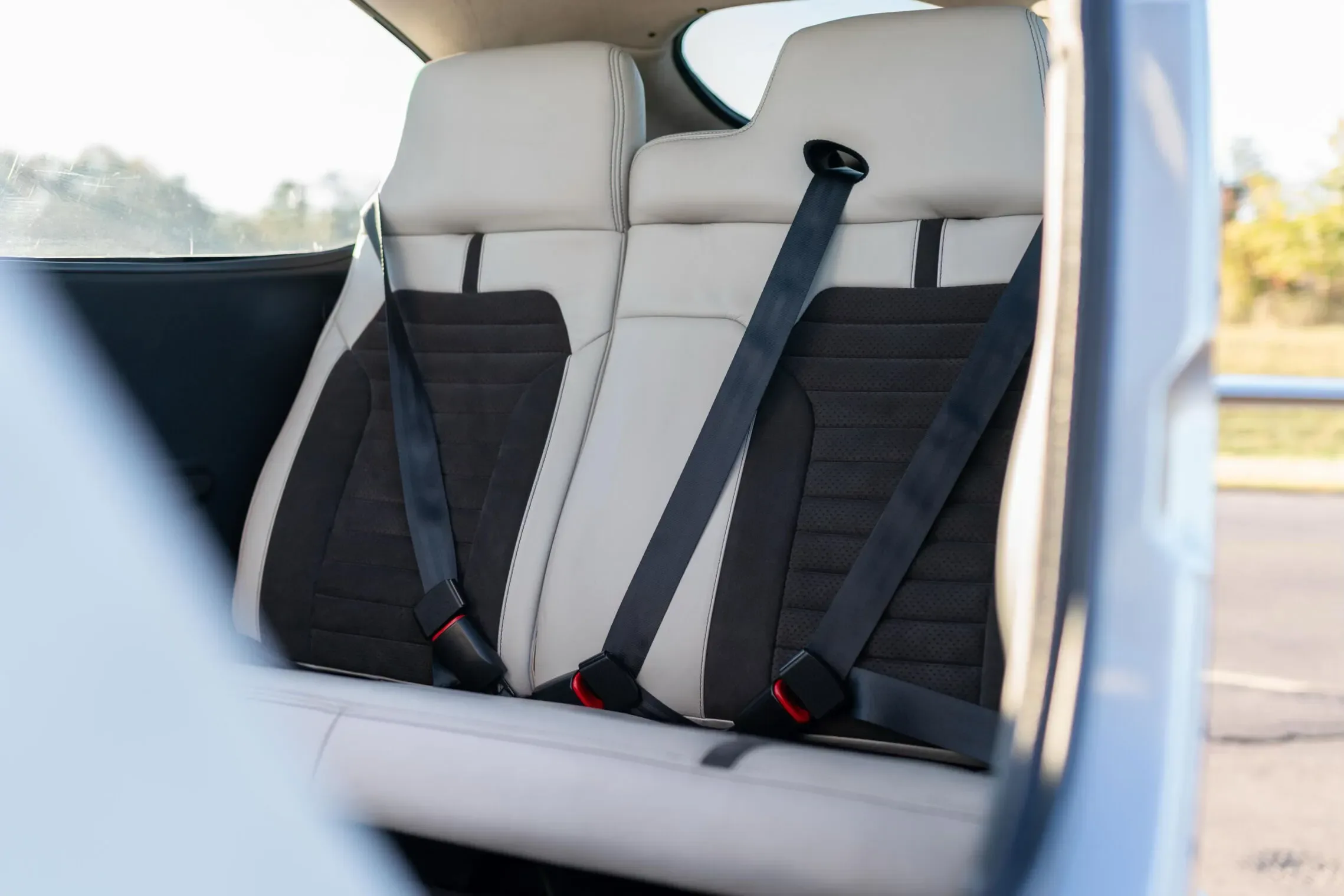 The two-tone white and black rear passenger seats with seatbelts inside the aircraft cabin.