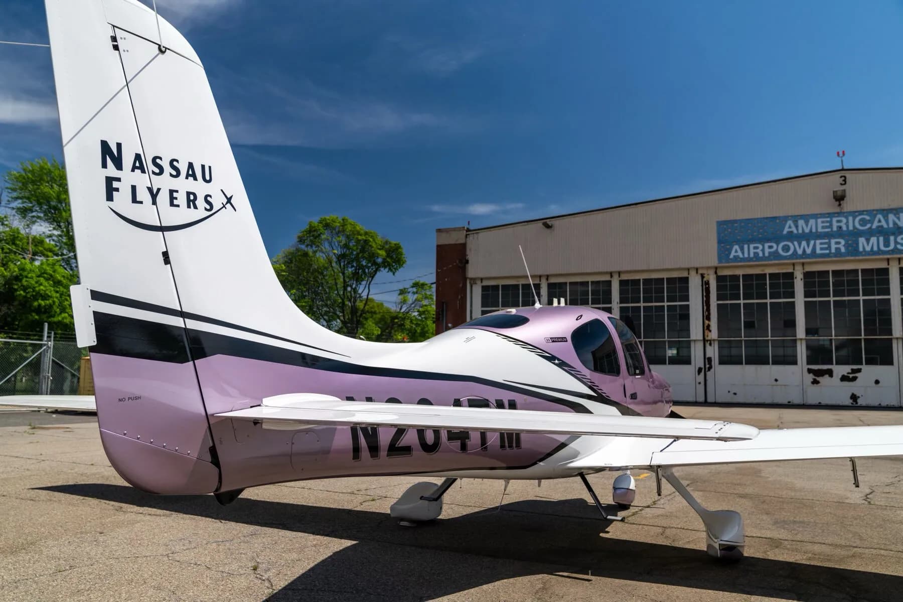 A rear three-quarter view of the metallic lavender and white Cirrus SR22 aircraft, registration N264TM, showing the tail and wing.