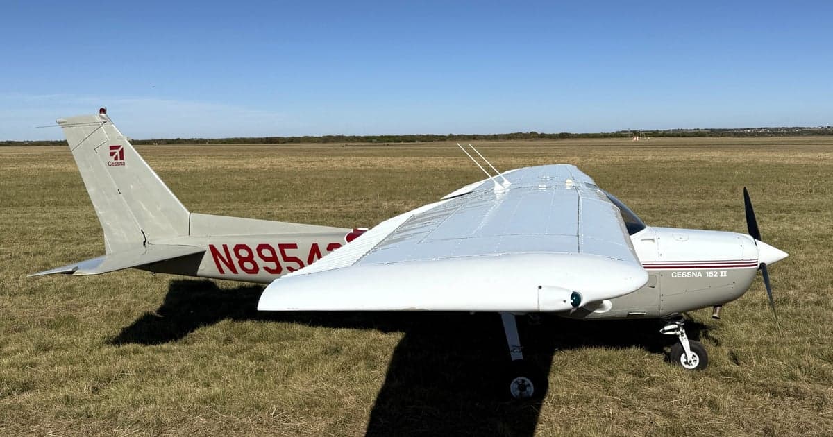 Side view of a Cessna 152 II aircraft with registration number N89543 parked on a grassy field.