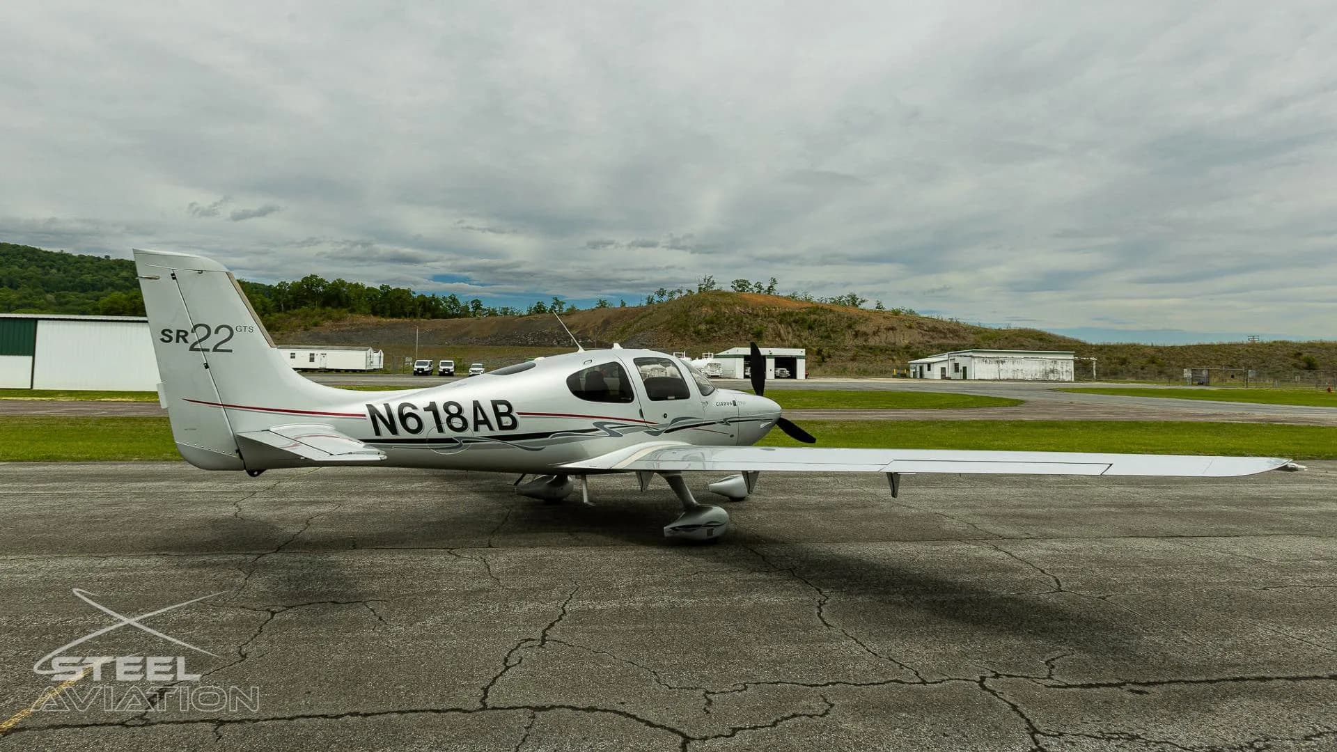 A silver Cirrus SR22 GTS aircraft with registration N618AB parked on an tarmac, viewed from the right side.