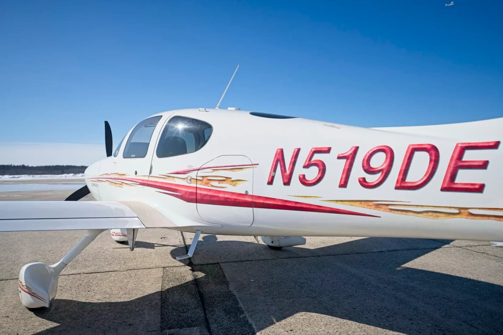 A close-up view of the fuselage of a white Cirrus SR22 aircraft, showing the N519DE registration and red and gold decals.