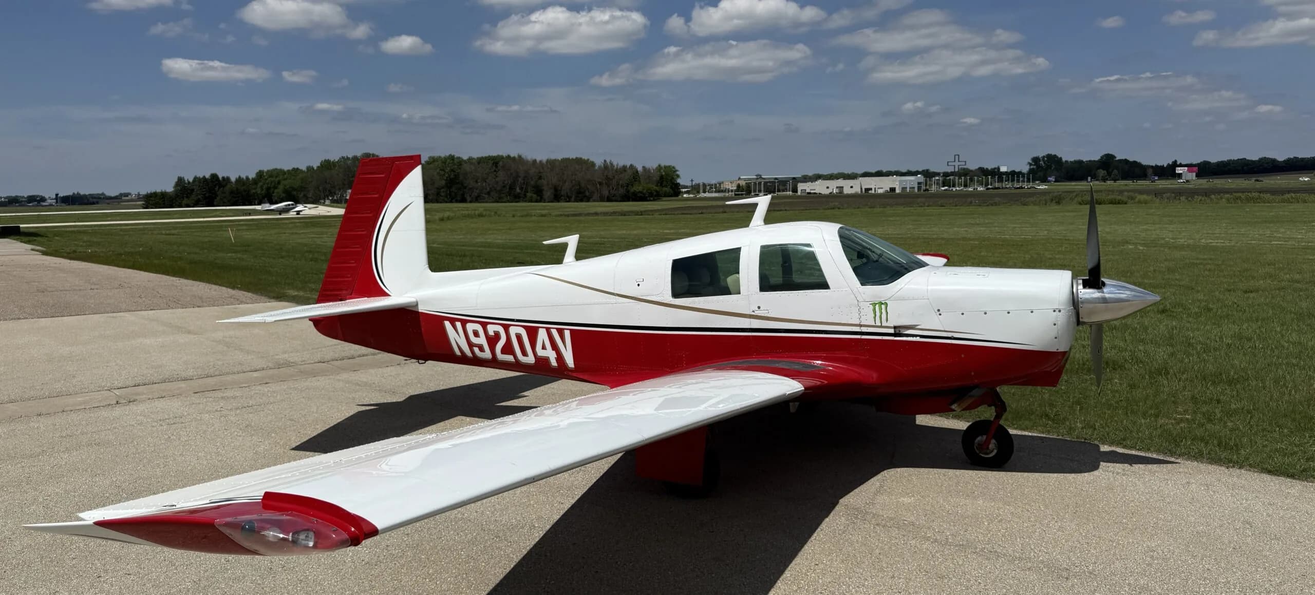 A white and red single-engine propeller aircraft with registration N9204V and a Monster Energy logo is parked on an airfield.