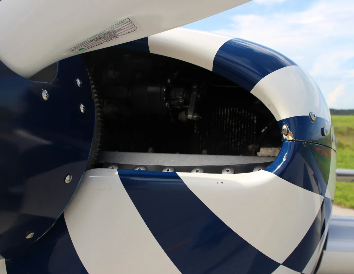 A close-up of the blue and white checkered engine cowling of the N51E Extra EA-300/L, revealing part of the engine.