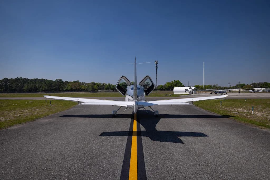 A rear view of the silver Cirrus SR22 aircraft N904BL with its doors open, centered on a runway.