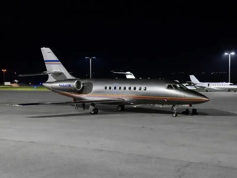 Side view of a Falcon aircraft with a silver and orange paint scheme on the tarmac at night.
