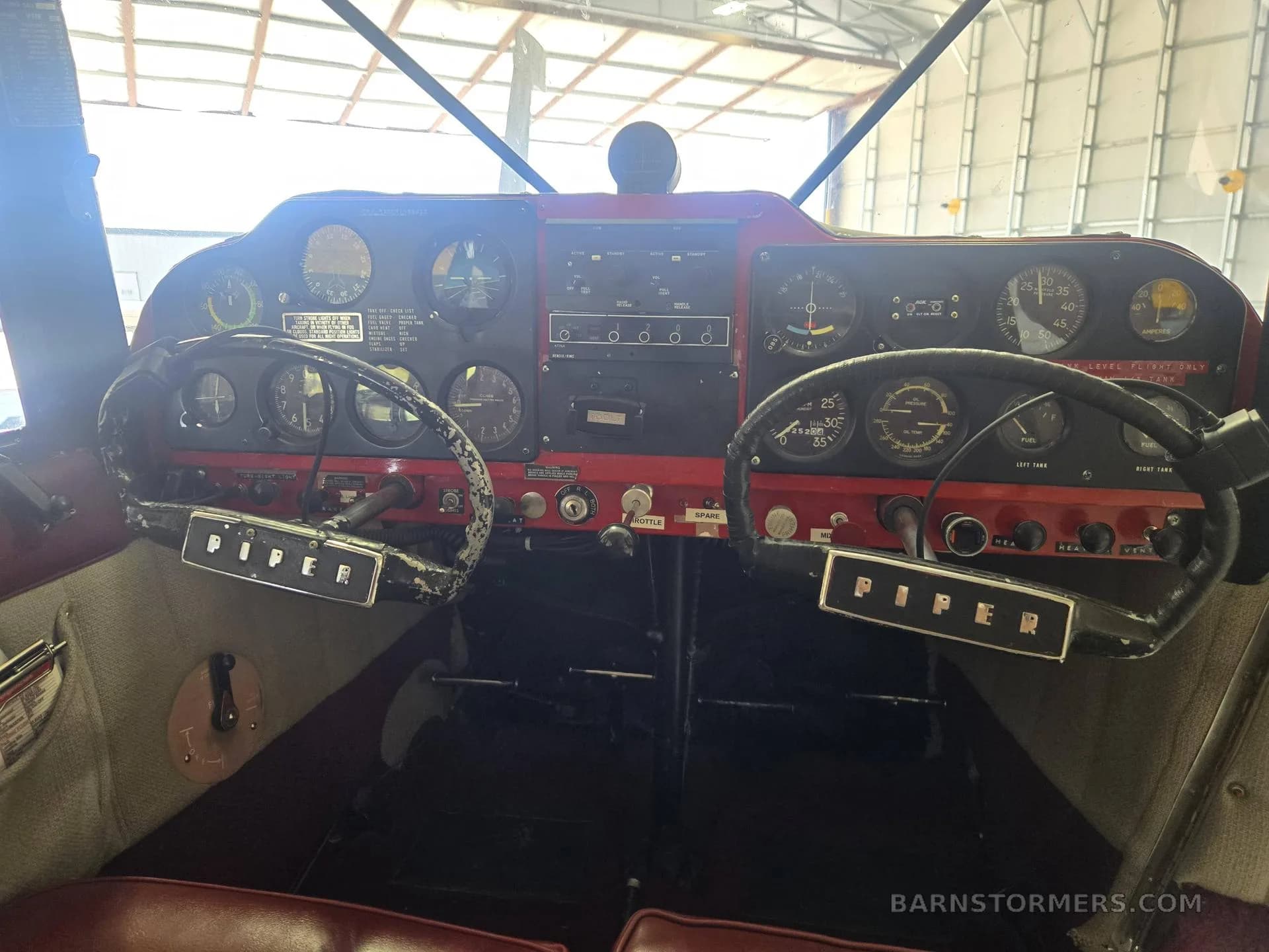 The cockpit of a Piper aircraft, showing the instrument panel, yokes, and controls.