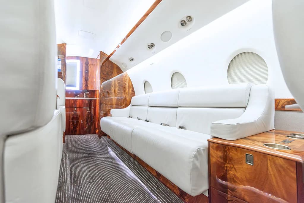 A close-up view of the white leather sofa and polished wood cabinetry in the private jet's cabin.