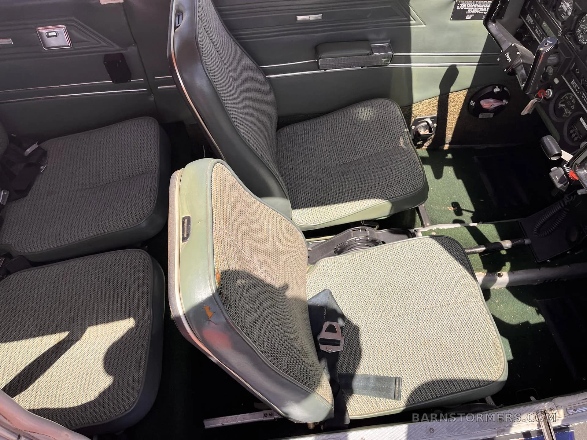 The interior cabin of an aircraft, showing green patterned fabric seats and dark green trim.
