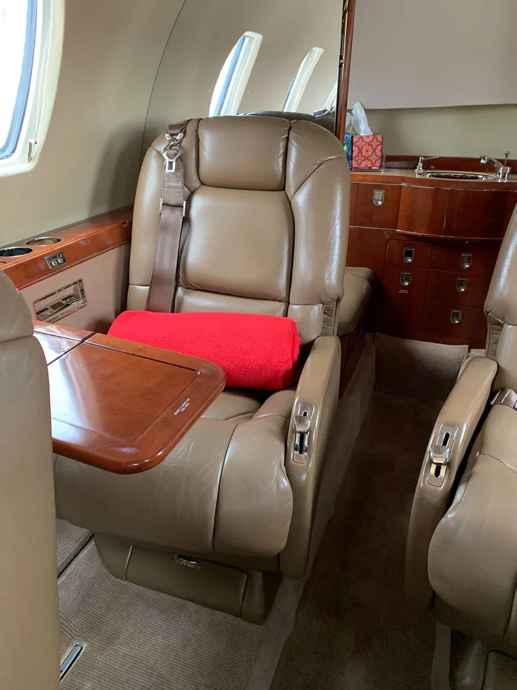 A tan leather seat with a red blanket and a fold-out table, with a wood-paneled cabinet in the background.