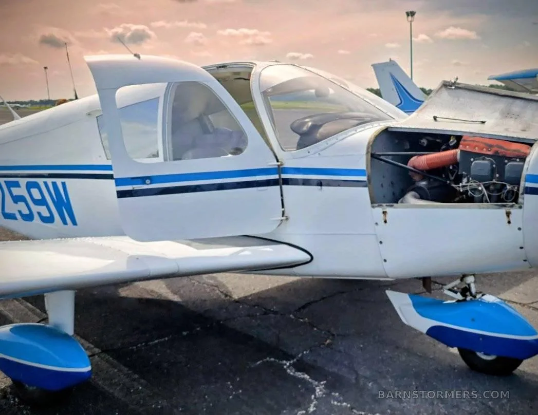 A white and blue light aircraft with open doors and engine cowling on an airfield.
