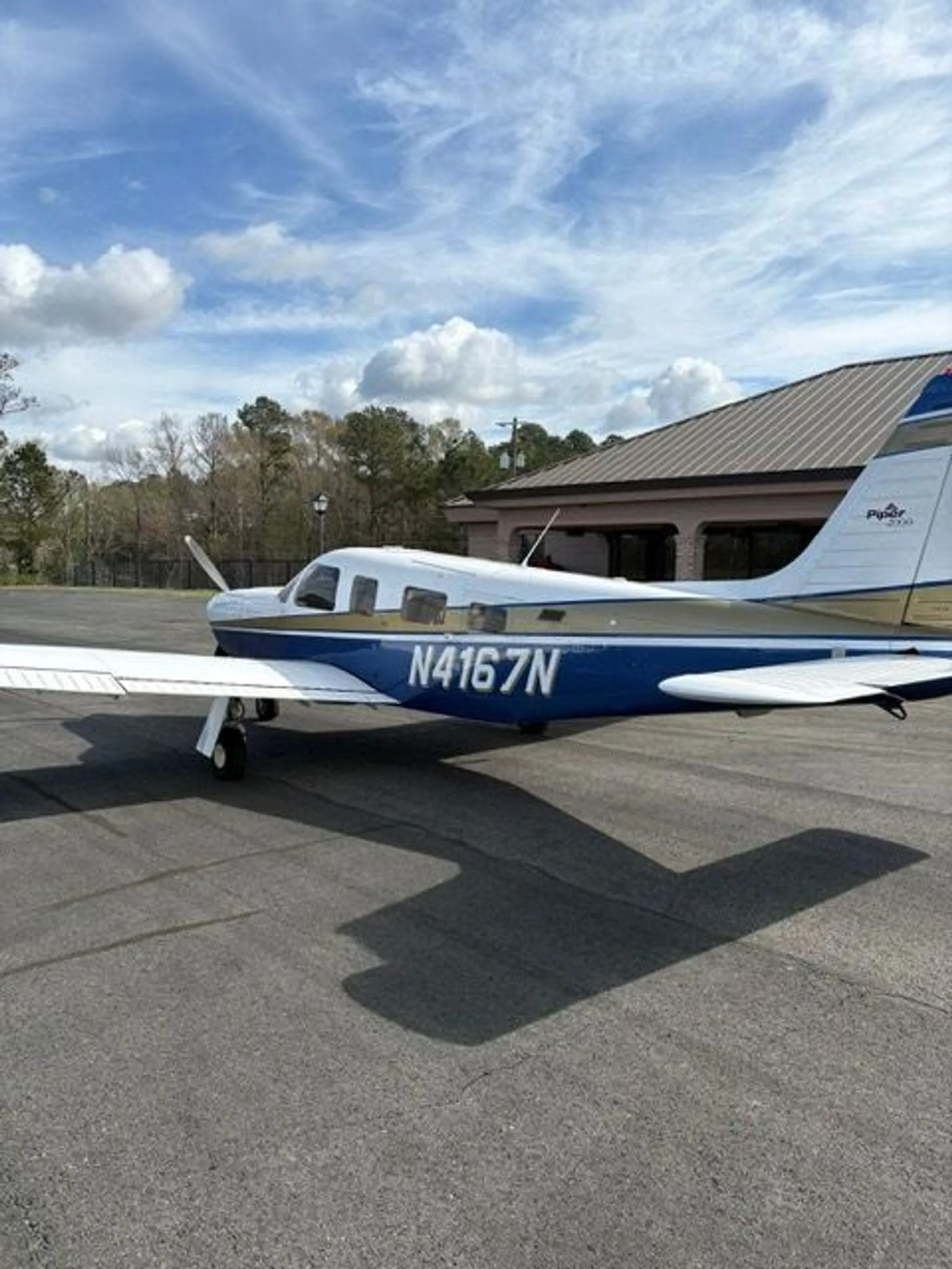 A side view of the Piper Saratoga II TC aircraft, N4167N, with white, blue, and gold paint, parked on an asphalt ramp.