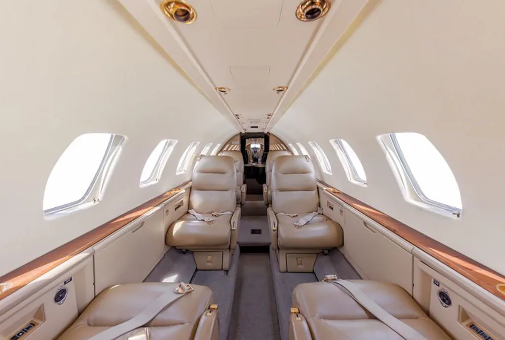 The interior cabin of a business jet, featuring light tan leather seats arranged in a club configuration.