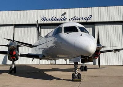 Front view of a white Beechcraft 1900C aircraft parked in front of a hangar.