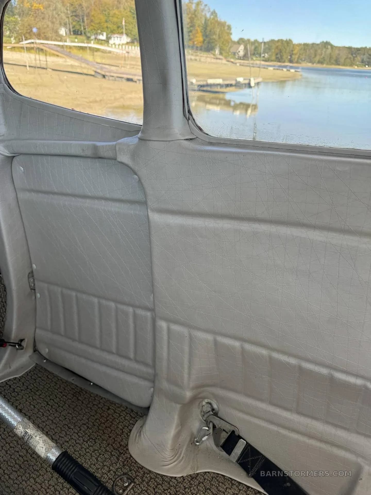 The light gray interior side panel and floor of the aircraft, with a view of a lake and shoreline outside the window.
