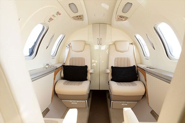 View of the interior cabin of a HondaJet with cream-colored seats and black pillows.