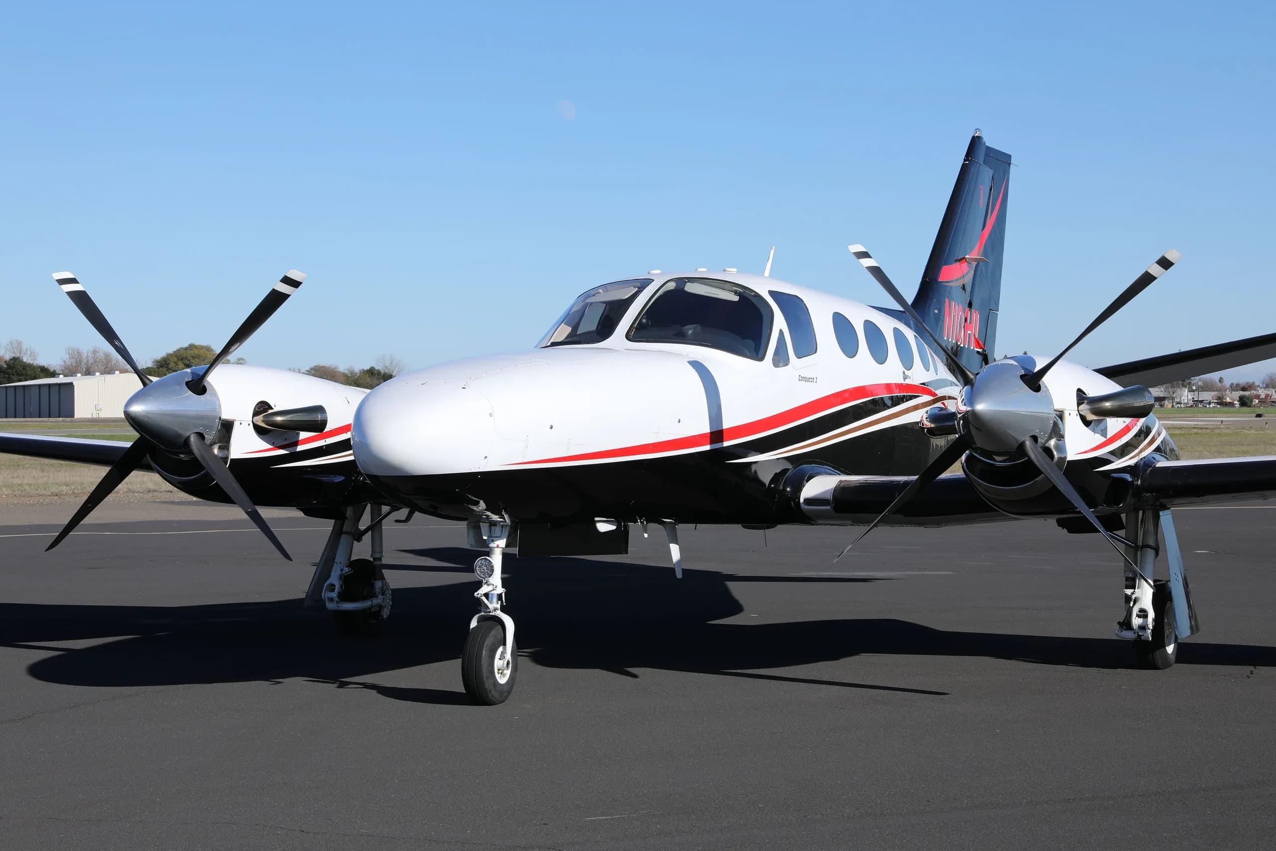 A front three-quarter view of the white, black, and red Cessna 414 Chancellor parked on an asphalt tarmac.