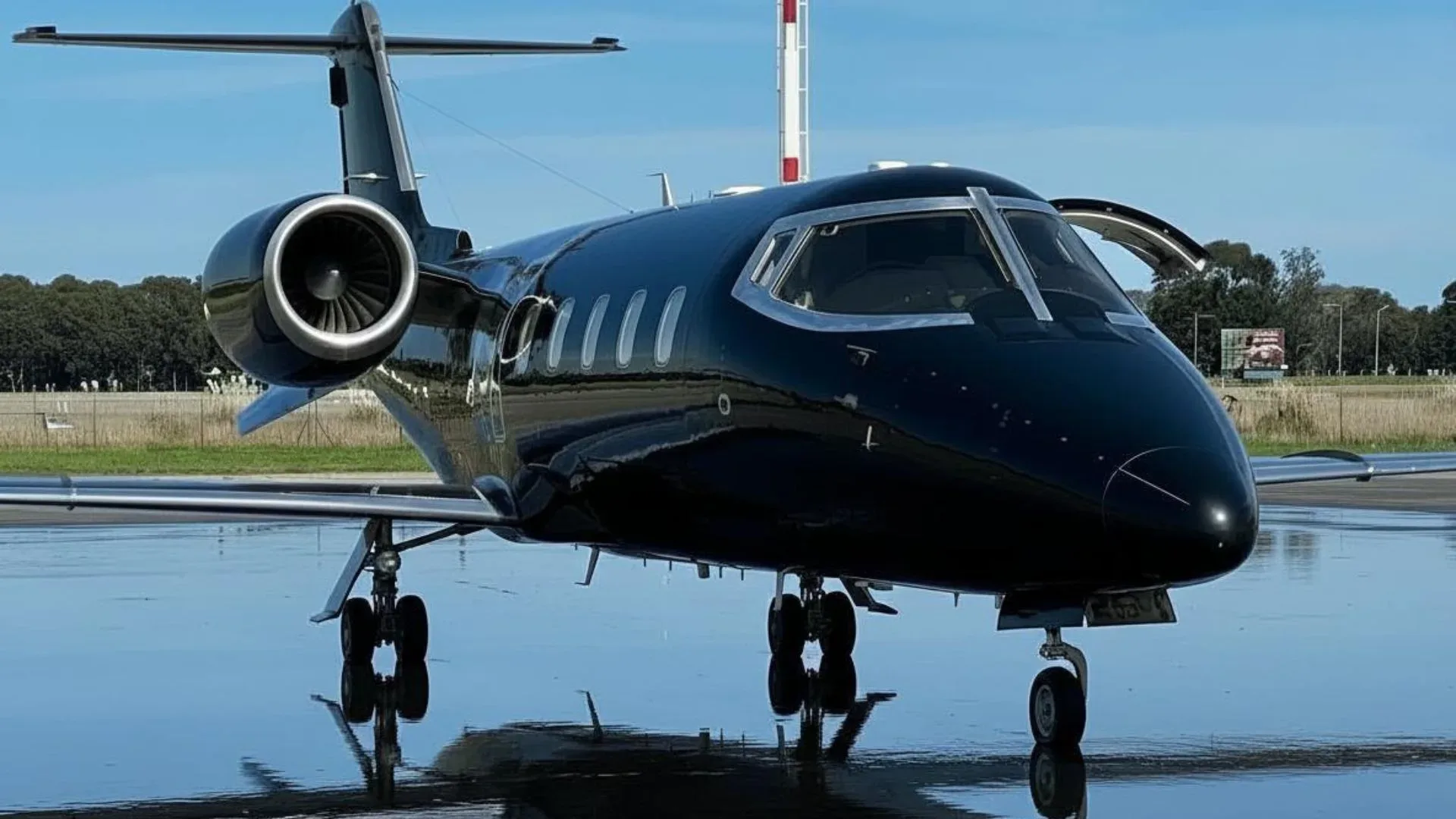 A black Learjet is parked on the tarmac with the door open.