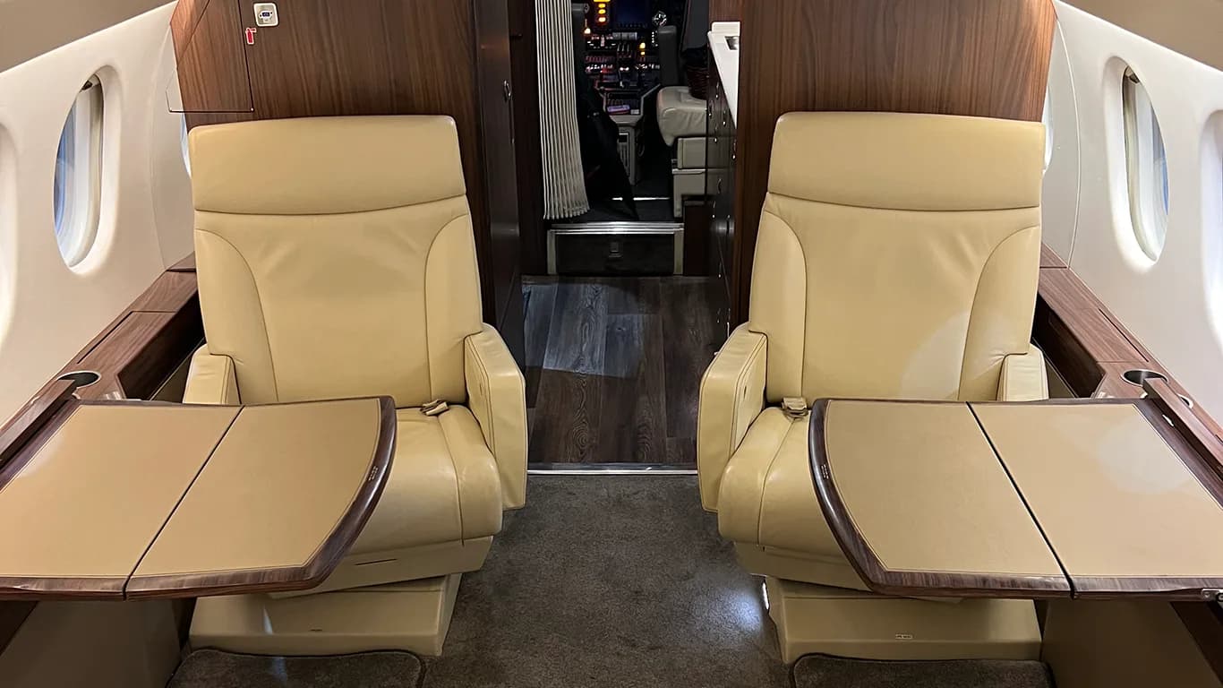 Two beige leather executive seats with fold-out tables face each other in the aircraft cabin.