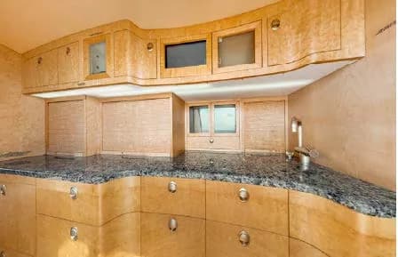 A well-appointed aircraft galley with light wood cabinetry, dark granite countertops, and a sink.